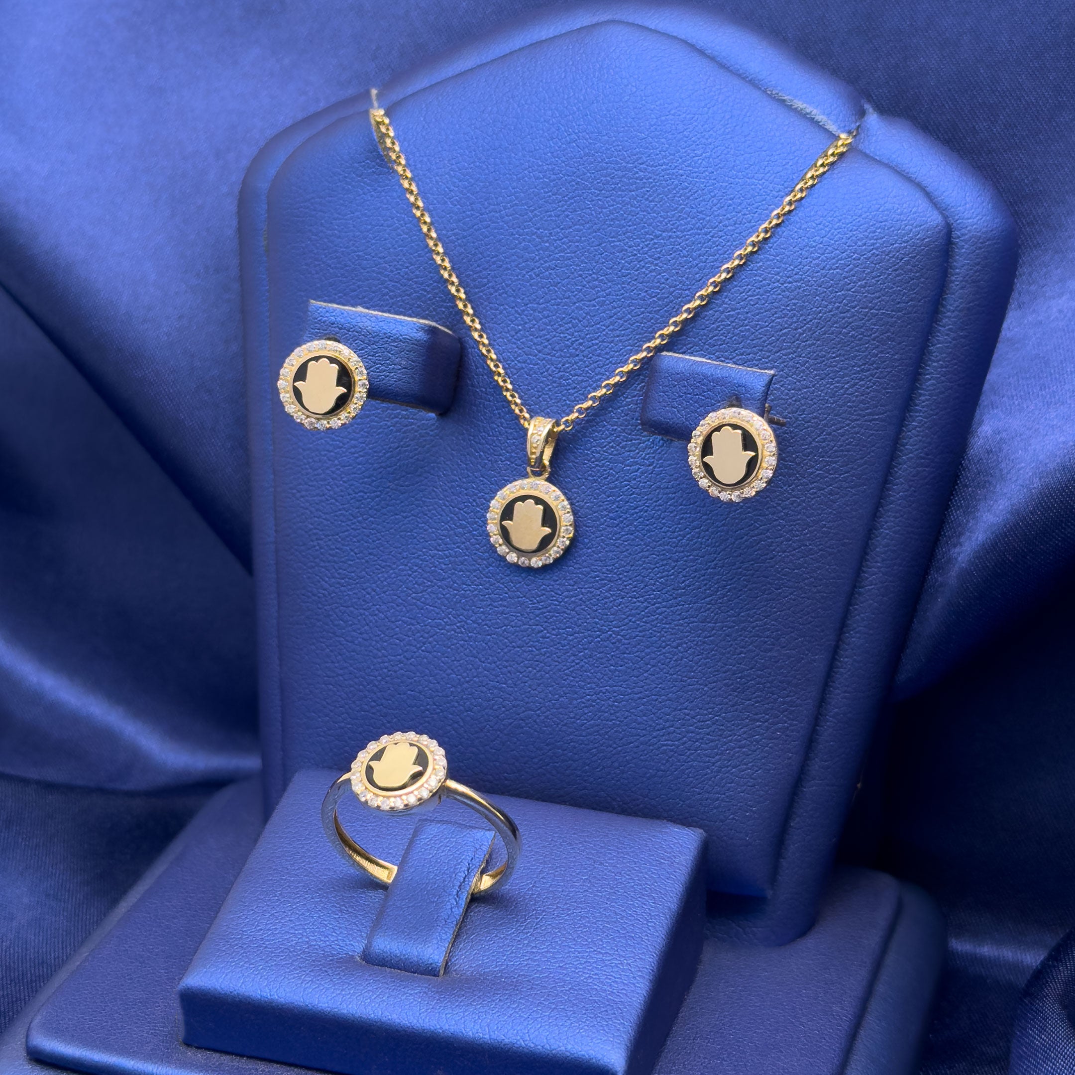 Gold jewelry set featuring a pendant necklace, matching stud earrings, and a ring, each with a circular medallion design, displayed on a blue jewelry stand.