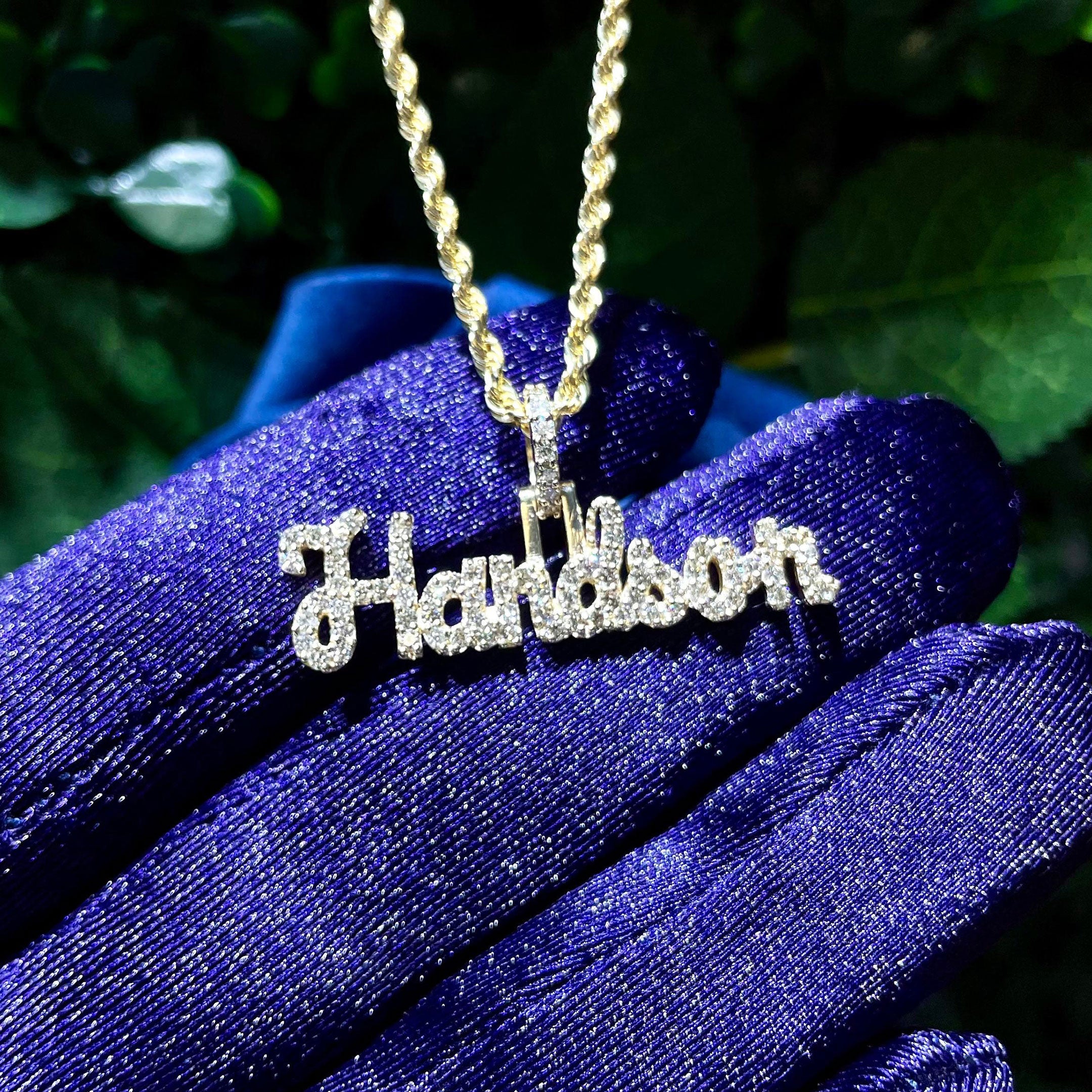 Gold necklace with 'Handson' pendant against a green leafy background close