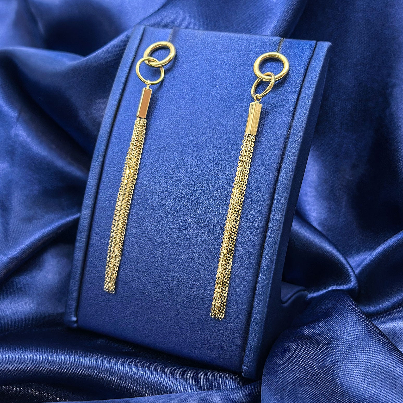 14k yellow gold hanging earrings with interlocking circles, rectangle bar, and multiple hanging chains on a jewelry display with blue background