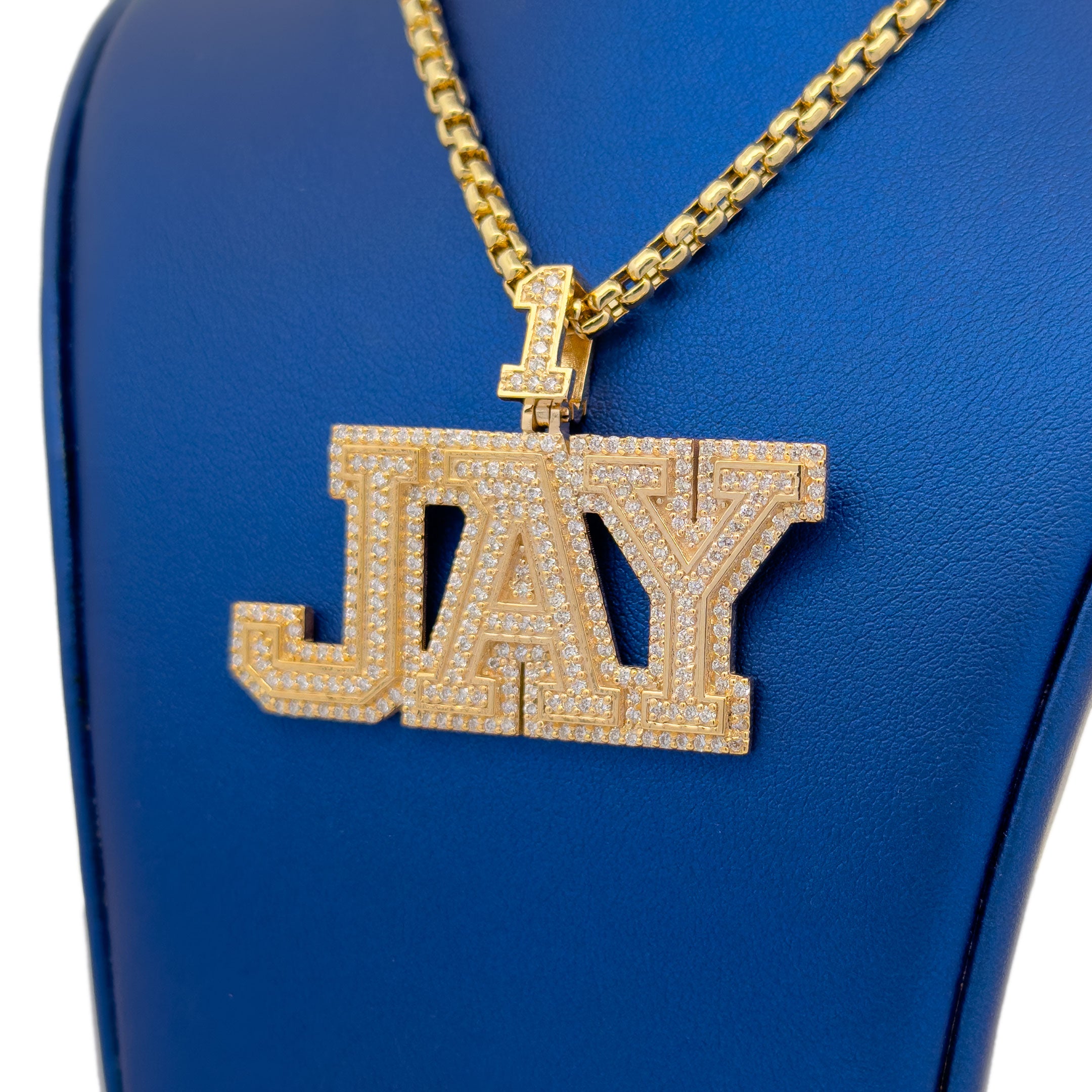Gold 'JAY' necklace pendant on a blue background