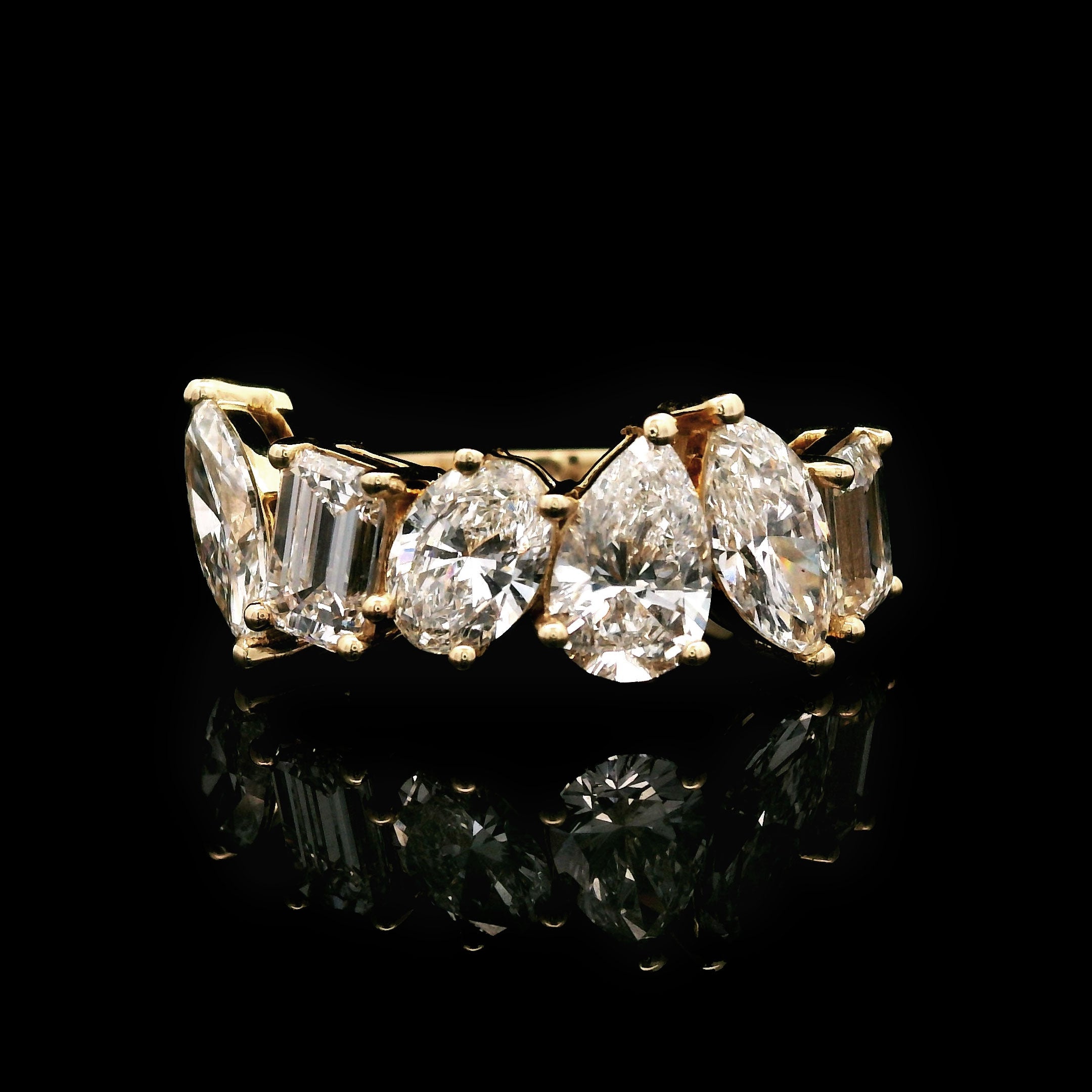 Gold wedding band with marquise, emerald, oval and pear shaped diamonds on a black background