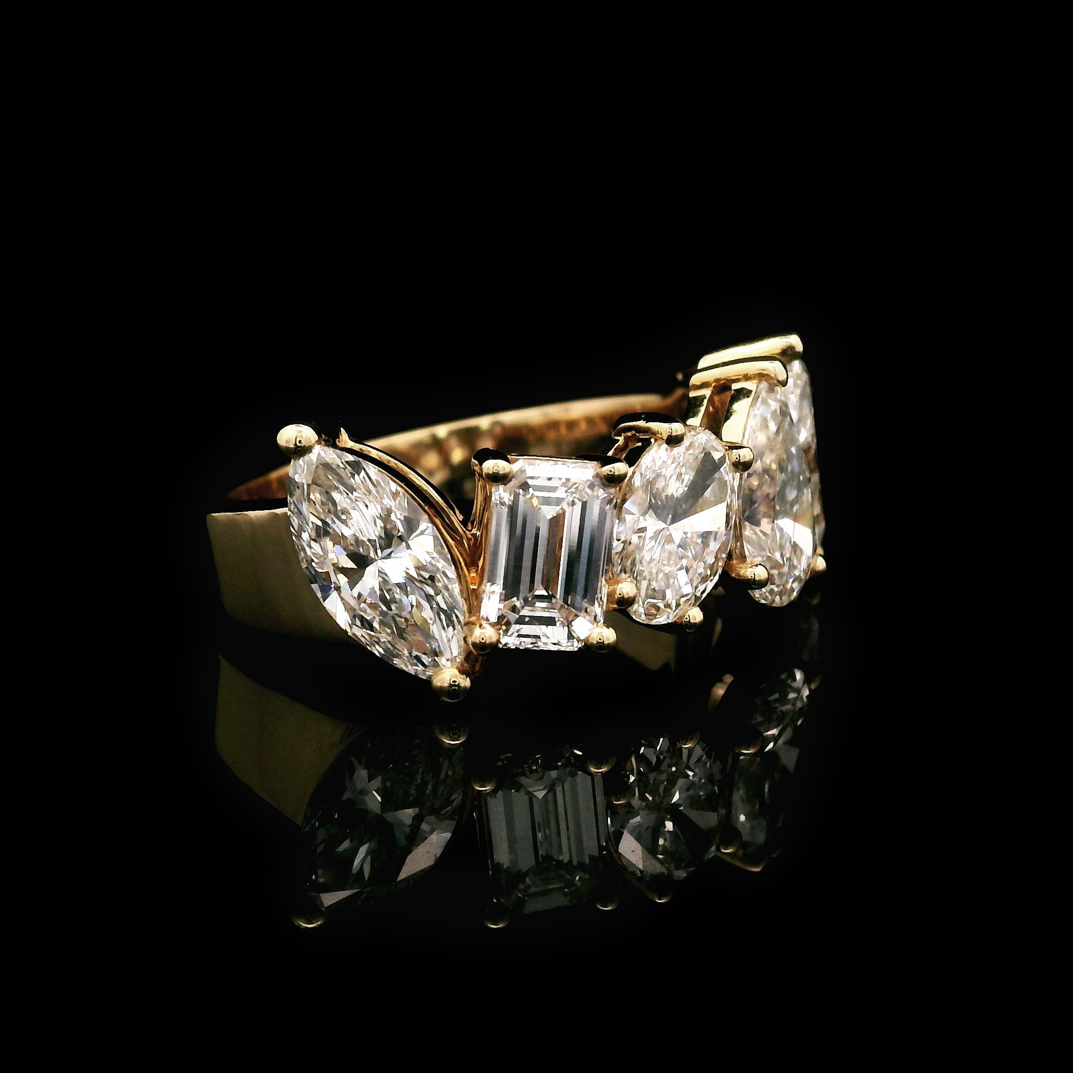 Gold wedding band with marquise, emerald, oval and pear shaped diamonds on a black background left