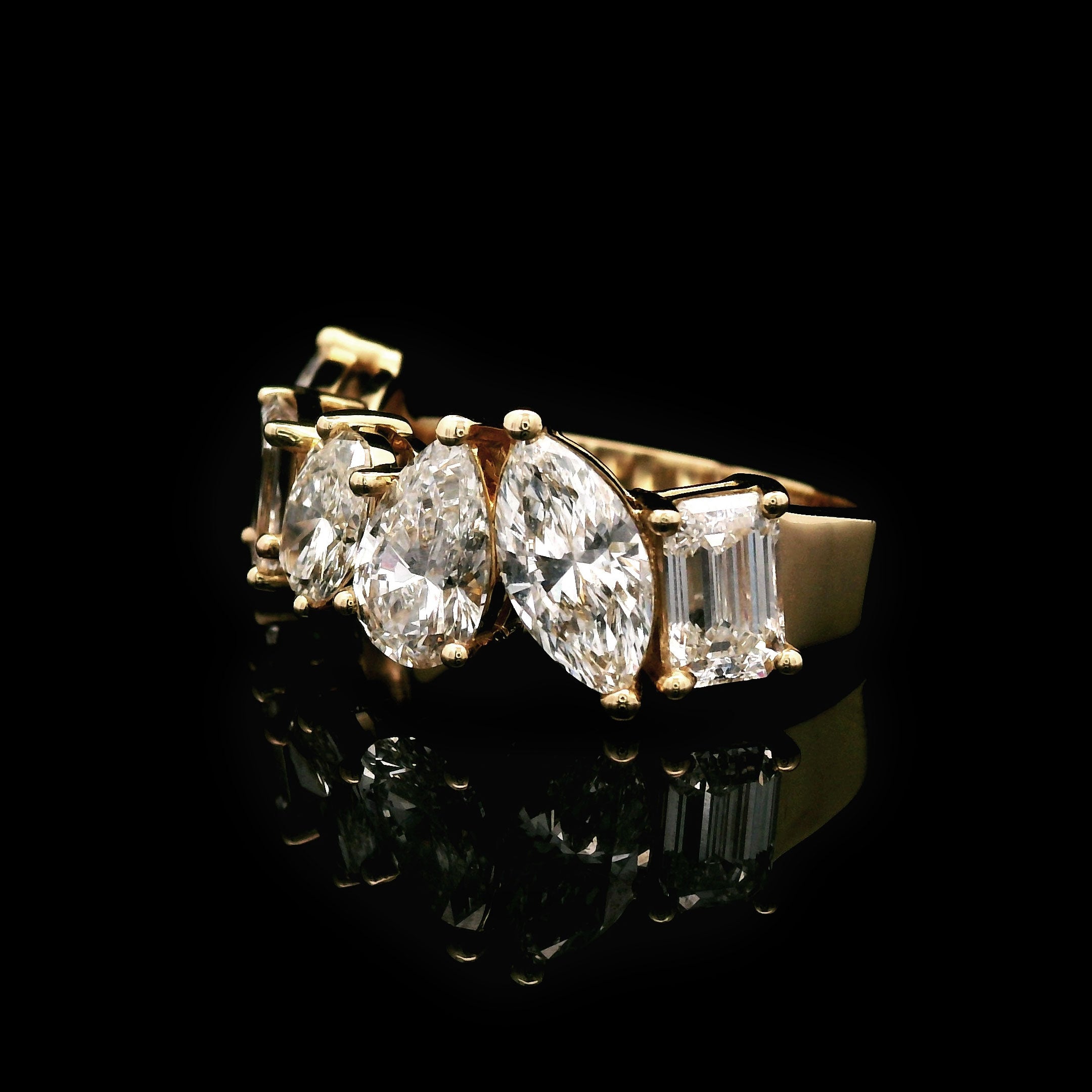 Gold wedding band with marquise, emerald, oval and pear shaped diamonds on a black background right
