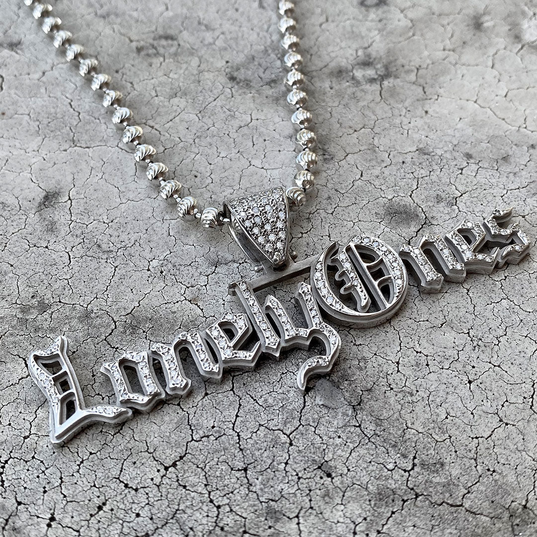 Silver necklace with 'Lonely Ones' pendant on a textured surface