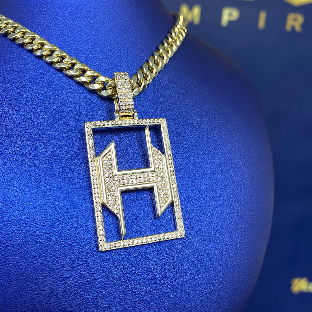 Gold chain with a diamond-encrusted 'H' pendant on a blue background