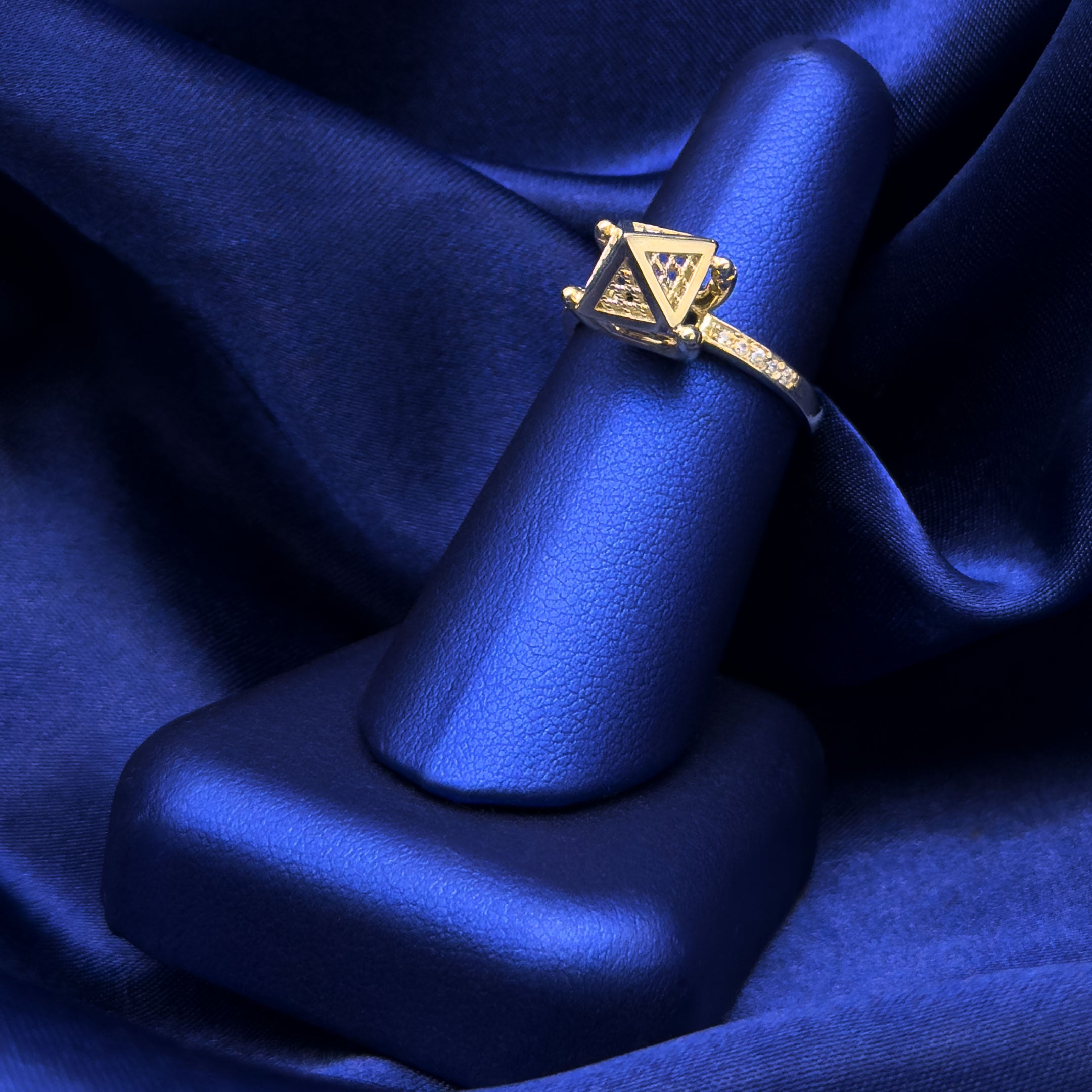 Gold ring with pyramid design on a blue finger jewelry display