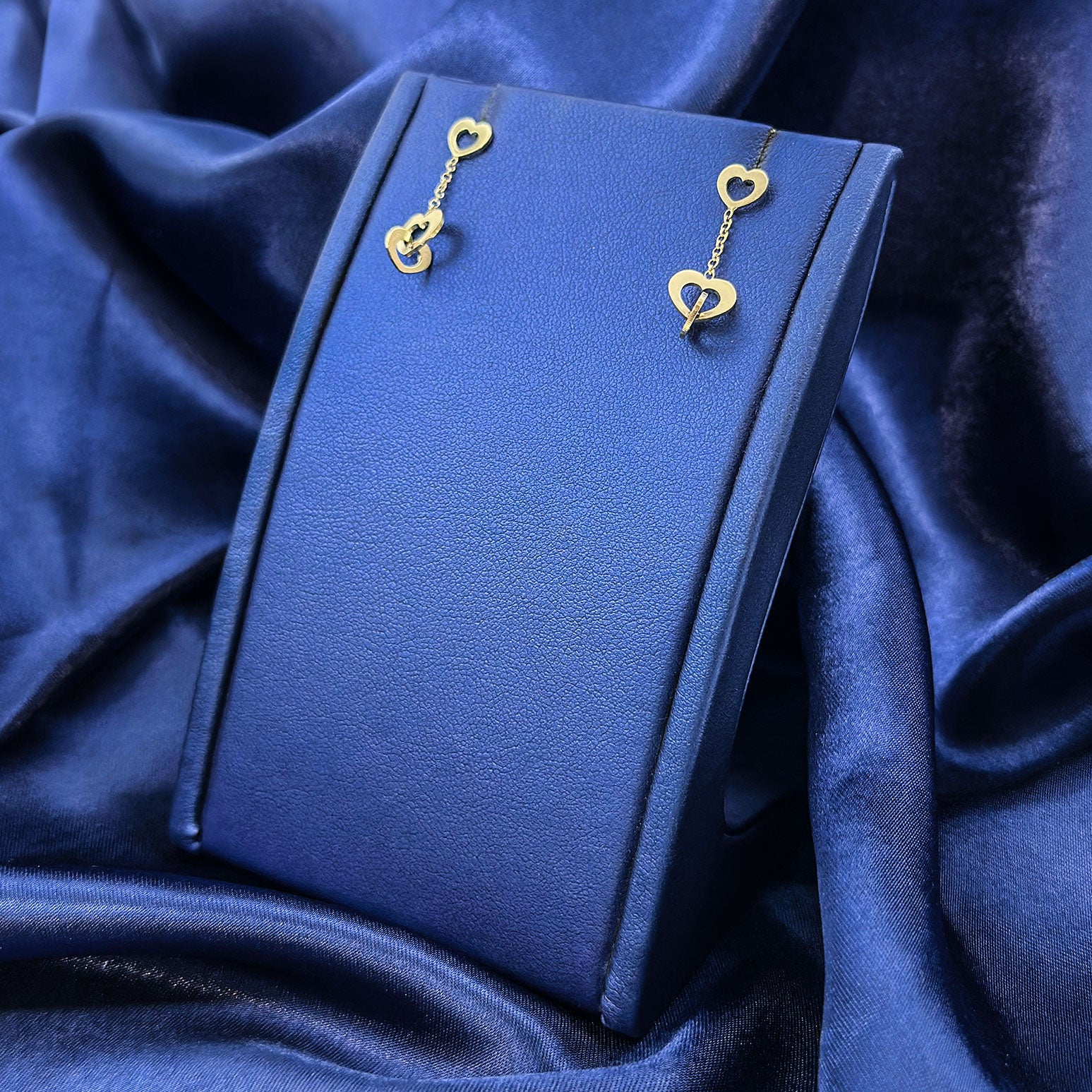 14k yellow gold triple heart and chain hanging earrings on blue earring display with blue background