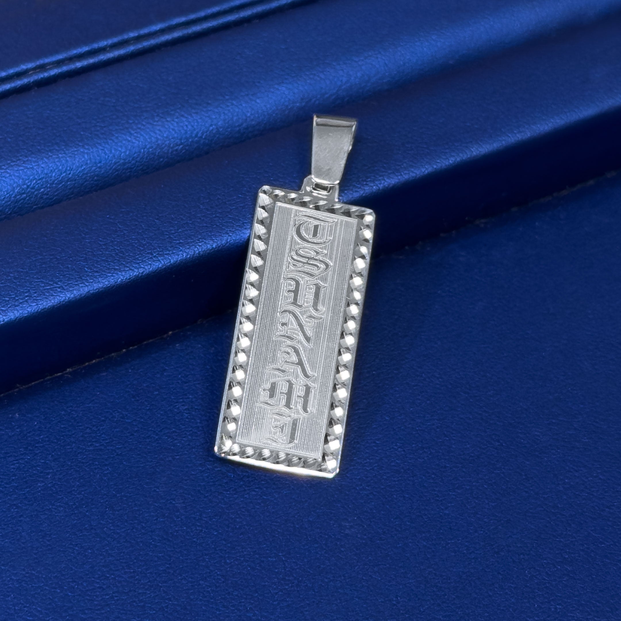 Silver pendant with engraved text on a blue satin background
