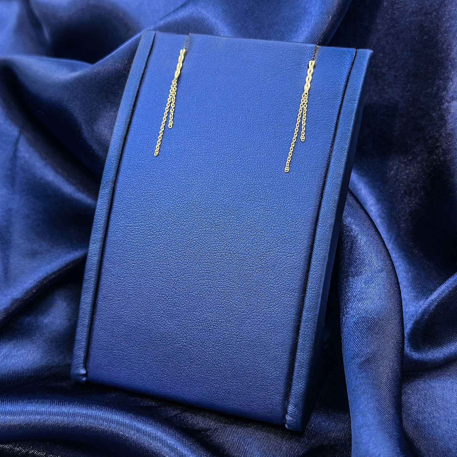 14k yellow gold twist and double chain hanging earrings on blue display with blue background