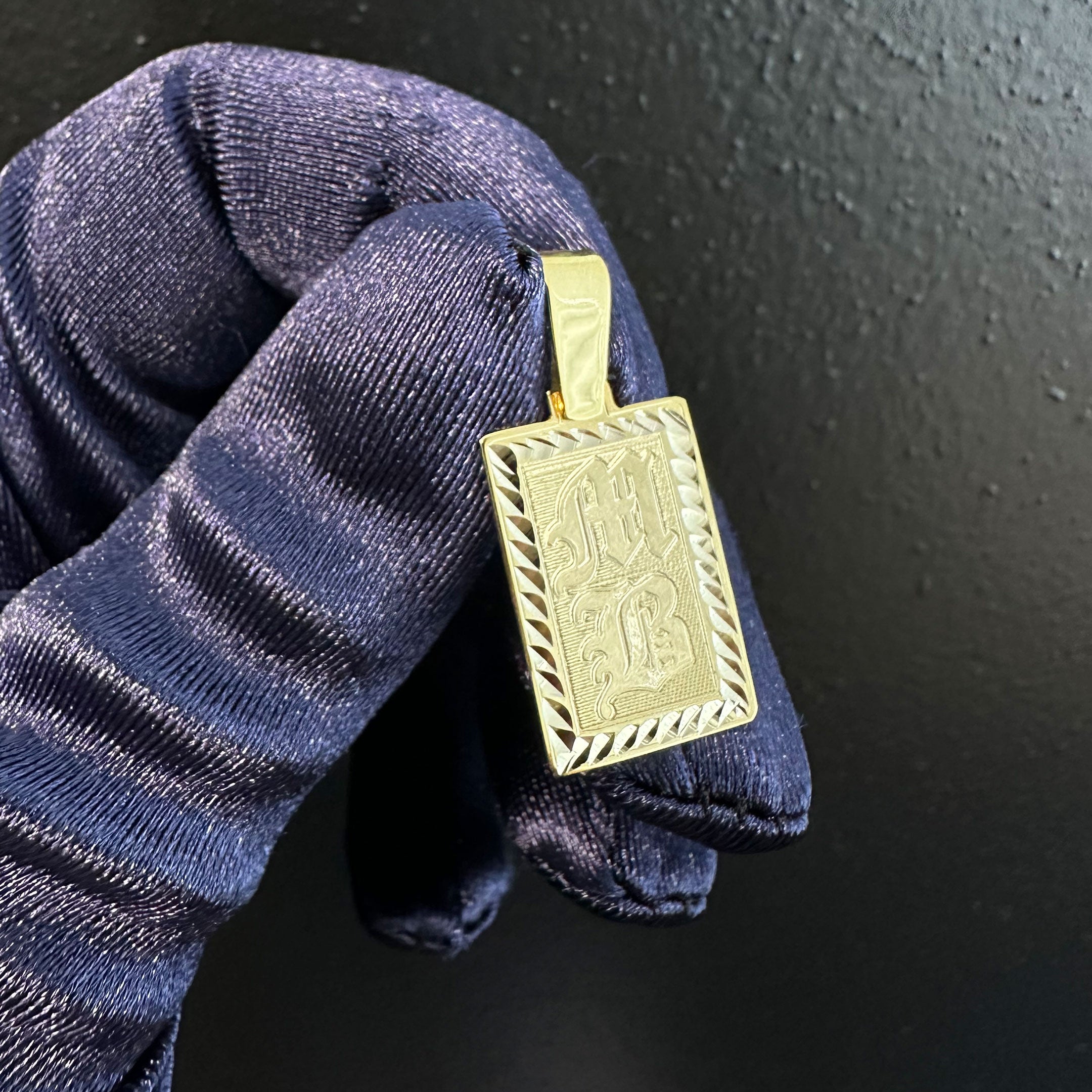 Gold rectangle pendant with diamond cut border and MB engraved in Old English in Hand with Blue Glove