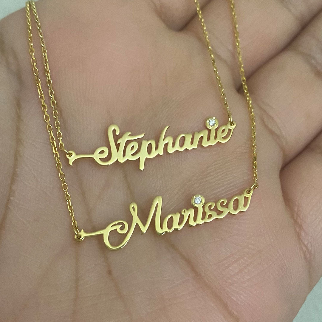Two personalized mini cursive name pendants with genuine diamond displayed in hand. Names Stephanie and Marissa.