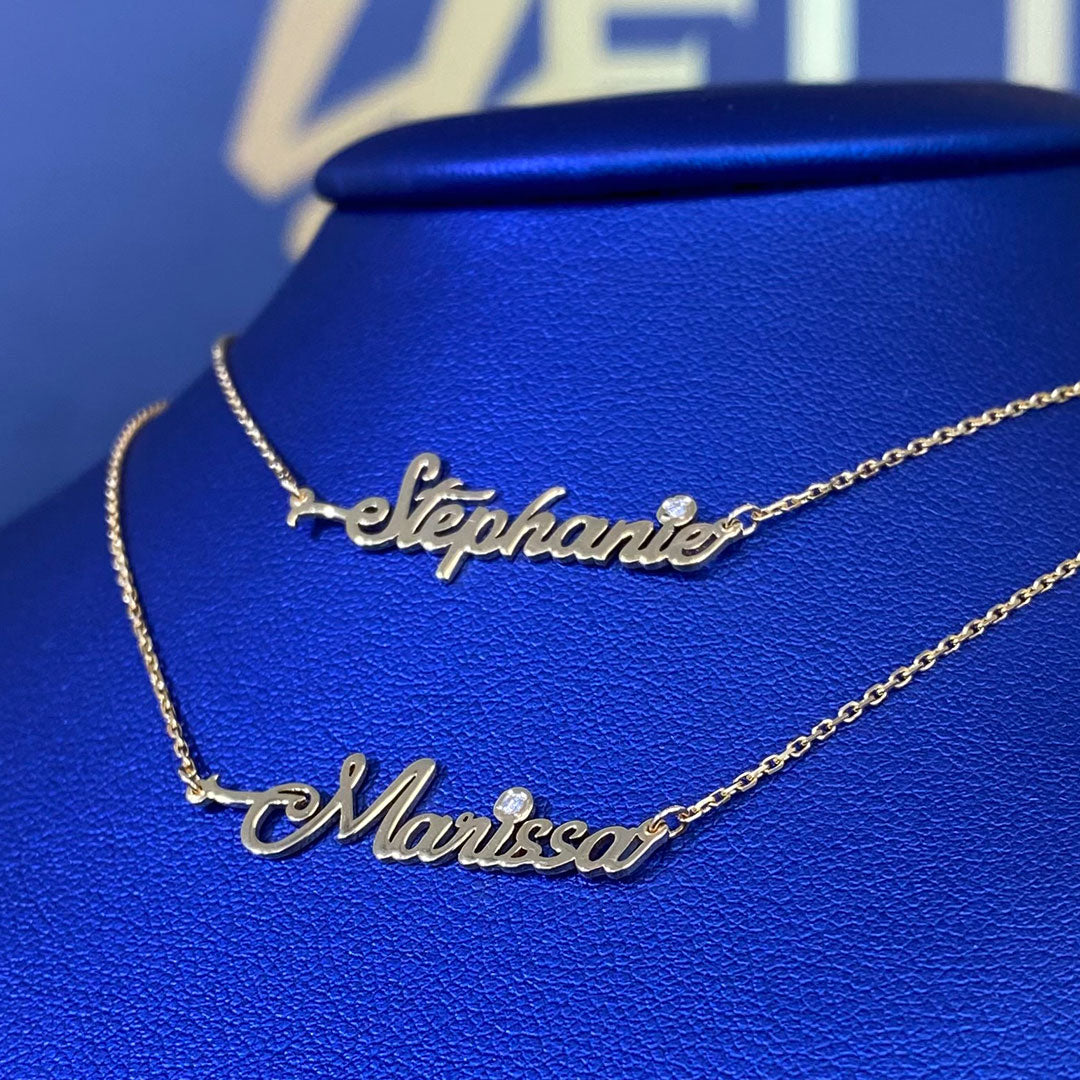 Two personalized mini cursive name pendants with genuine diamond displayed on a blue mannequin bust. Names Stephanie and Marissa.