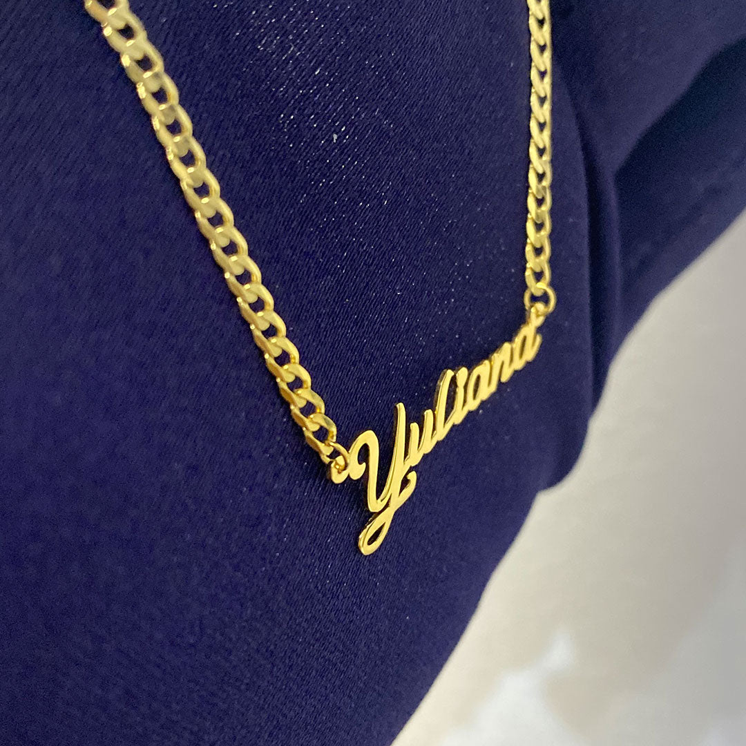 A yellow gold mini pendant with the cursive text 'Yuliana' held in a hand against a blue background. close