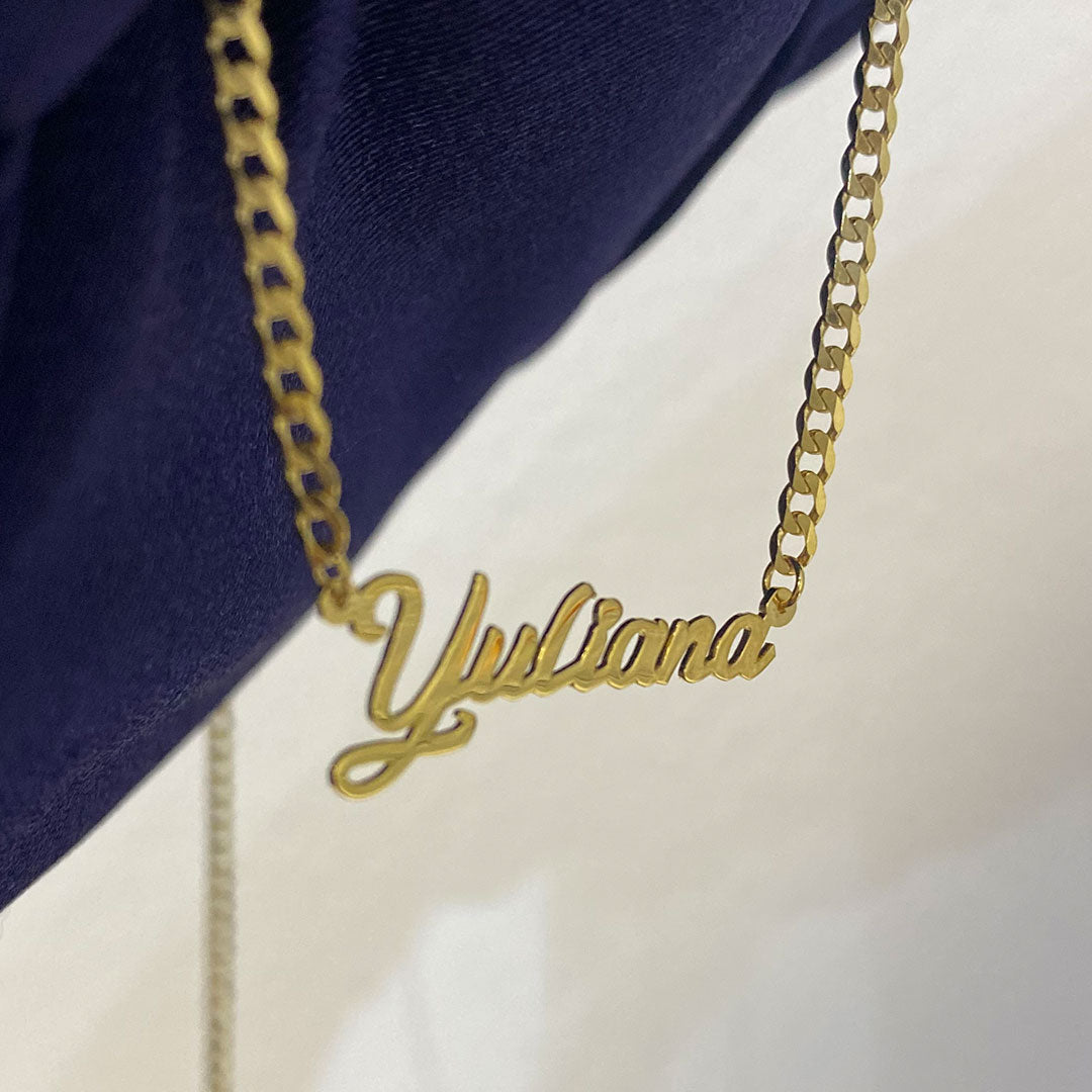 A yellow gold mini pendant with the cursive text 'Yuliana' held in a hand against a blue background. close